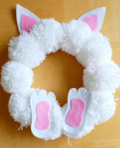 A cute handmade wreath made of white pom poms with a bunny motif